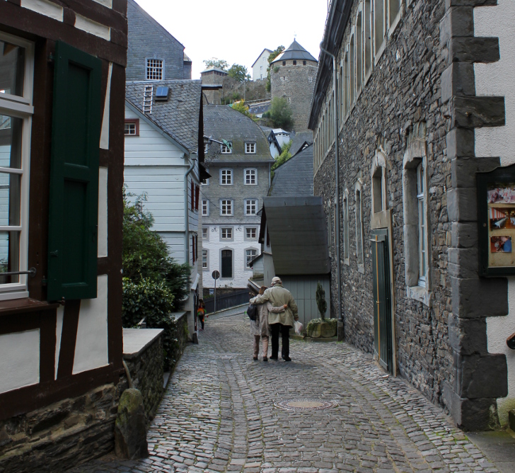 Das Foto zeigt eine Altstadt und zwei Menschen die Arm in Arm die Straße entlang gehen